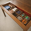 Board game accessories organized inside removable wooden storage compartments