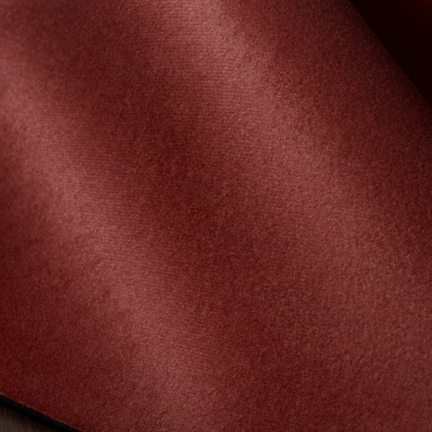 A close-up of a textured fabric material in a deep burgundy red color, showing the fine weave and soft folds.