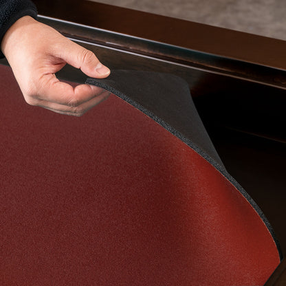 A close-up of a hand lifting a dark red upholstered cushion or pad to show its black textured backing, set against a dark wooden furniture surface.