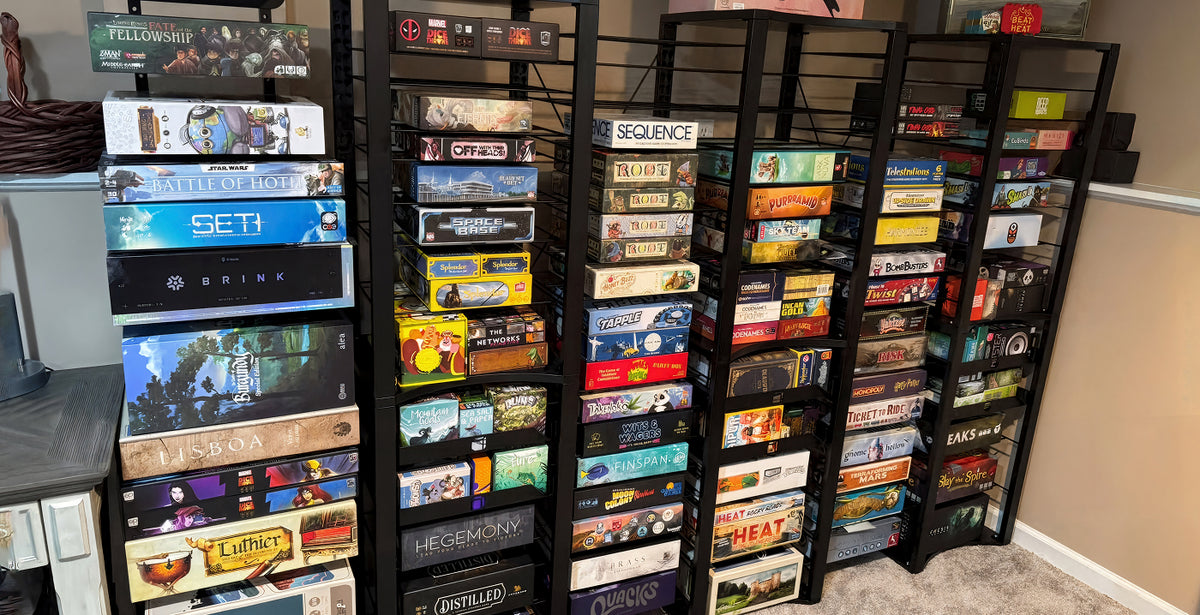 A set of black shelving units filled with board game boxes in a home office or playroom setting.