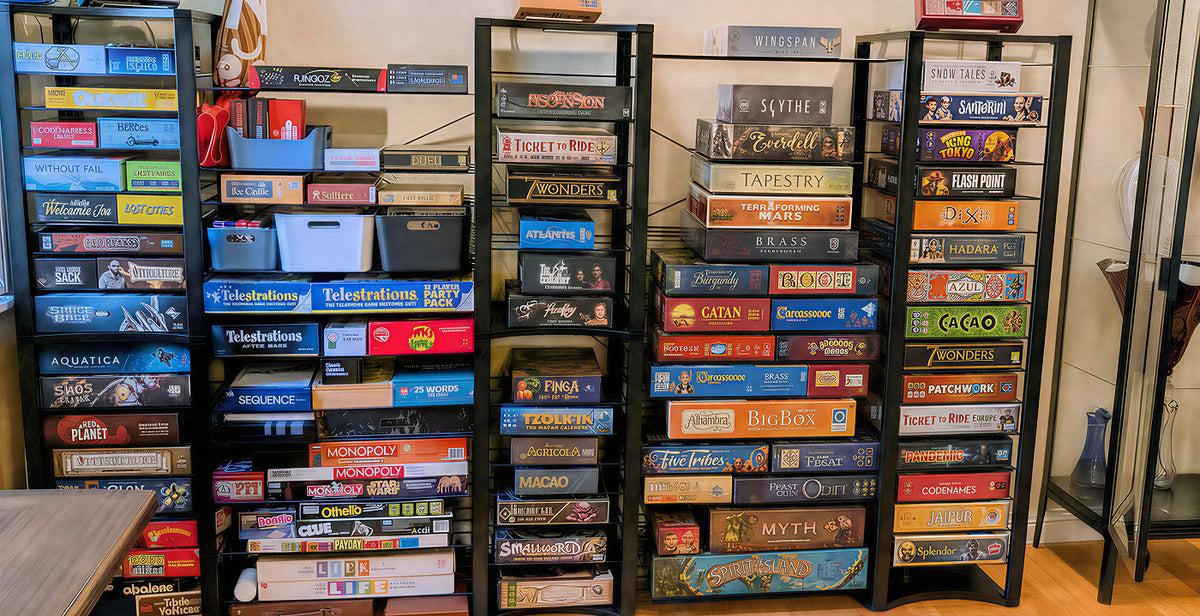 black metal shelving units filled with board game boxes in a home setting, with a table and room interior visible.