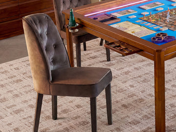 A brown velvet upholstered dining chair with button tufting on the back, shown beside a wooden game table
