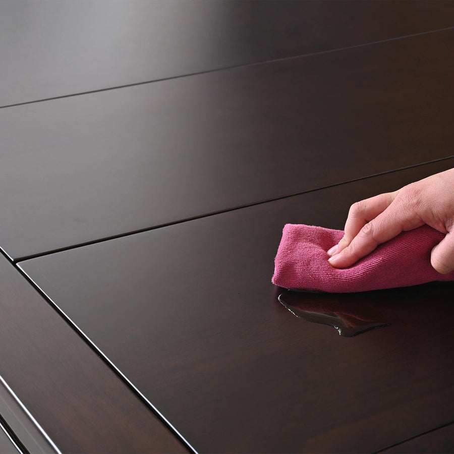 Hand wiping a spill from the dark brown, sleek Kingswood rubberwood game table with a pink cloth.