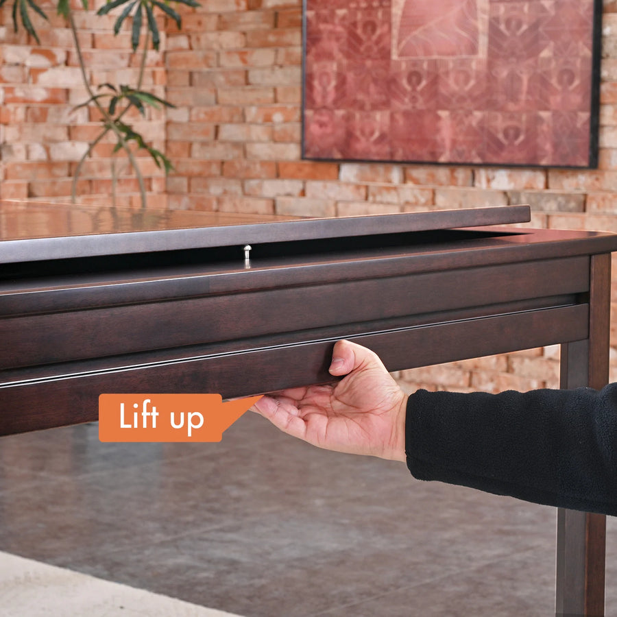 Hand lifting the dark brown rubberwood Kingswood game table's top to reveal its rail system.